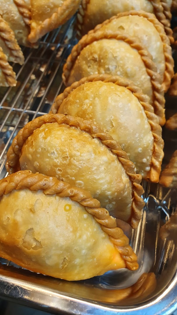 A close-up view of several golden-brown, braided pastries, likely curry puffs, arranged on a metal tray.