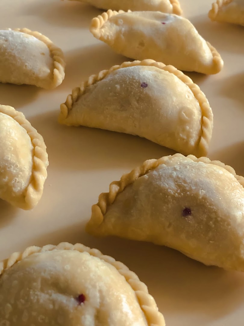 Close-up of several golden-brown pastries with crimped edges, possibly curry puffs or empanadas, on a light surface.