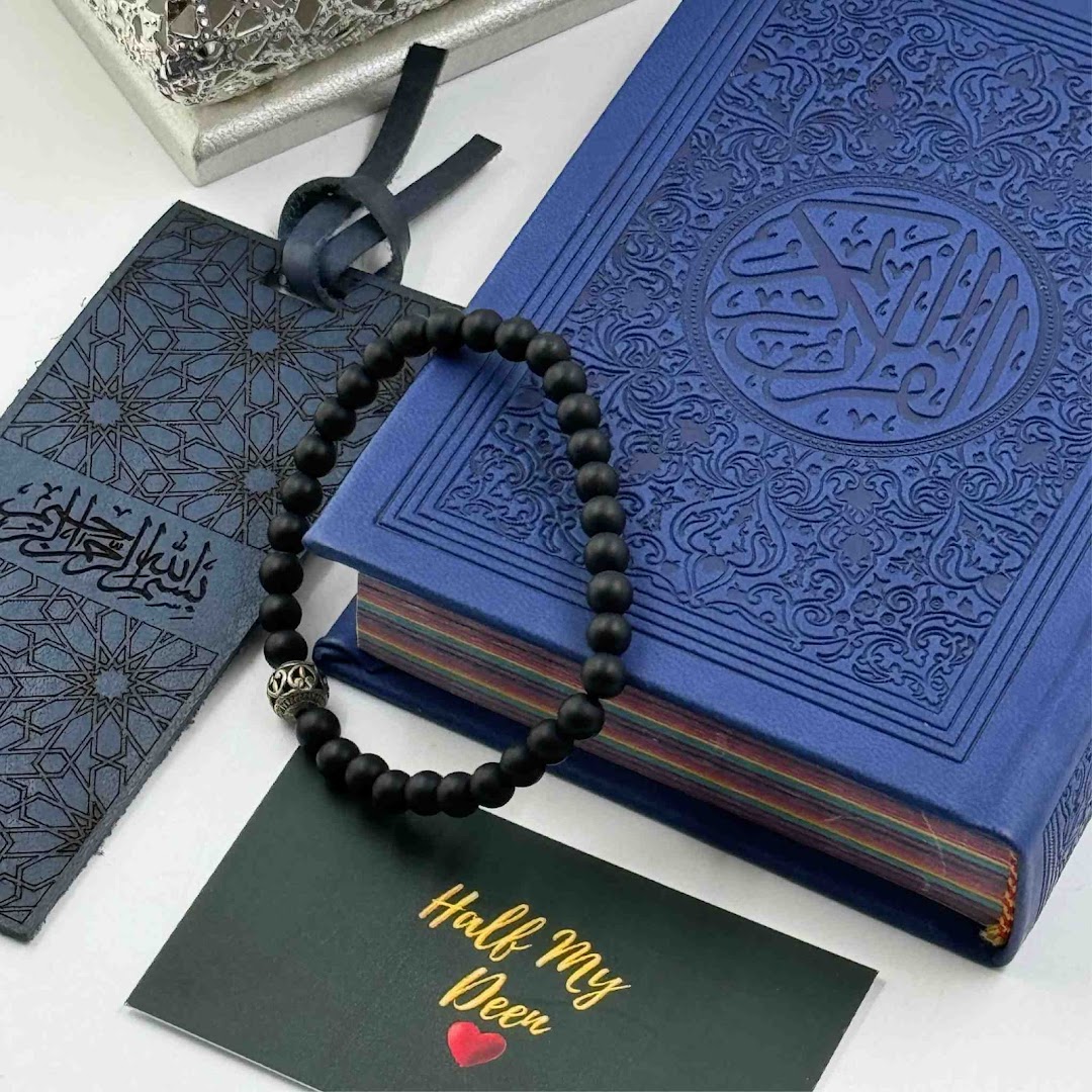 A blue Quran, black prayer beads, and a bookmark with a card on a white surface.