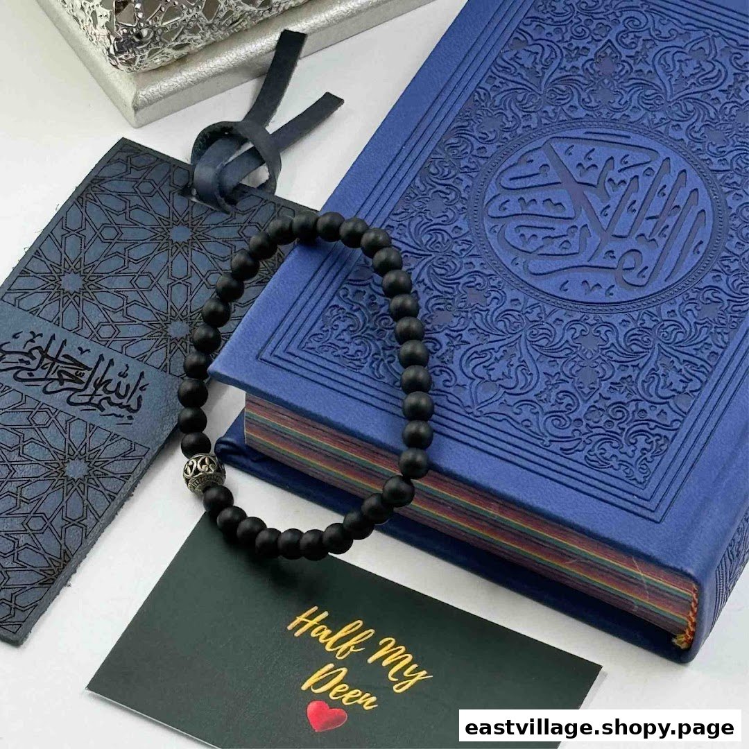 A blue Quran, black prayer beads, and a bookmark with a card on a white surface.