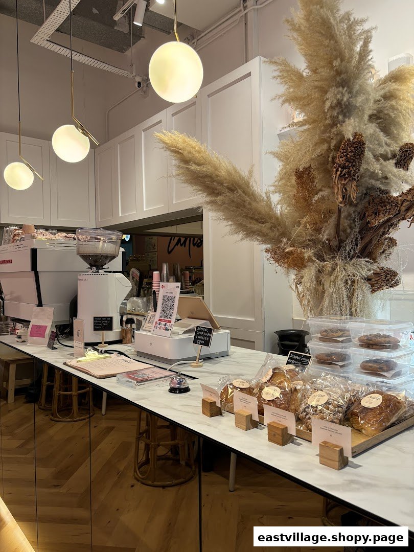 A well-lit coffee shop counter featuring coffee machines, pastries, and decorative pampas grass.