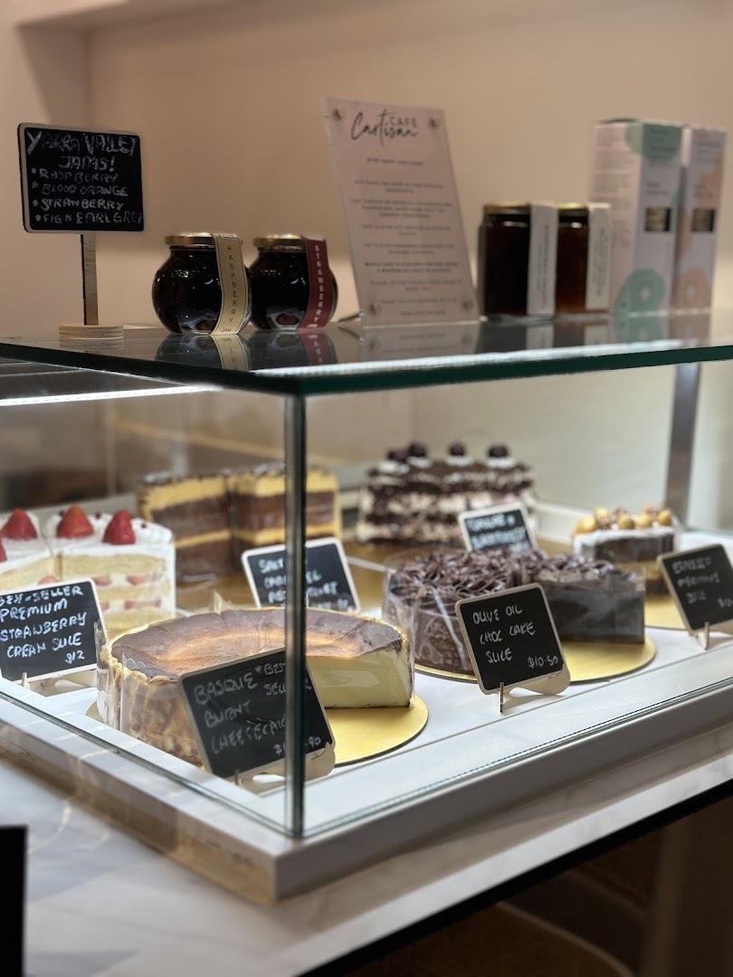 A display case showcasing a variety of delicious cakes and artisanal jams at Café Cartisan.