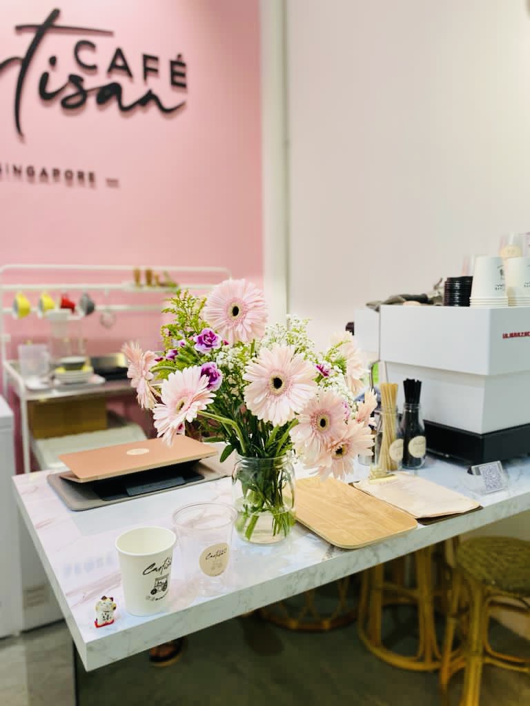 A cozy counter at Café Cartisan featuring a fresh flower bouquet and coffee essentials.