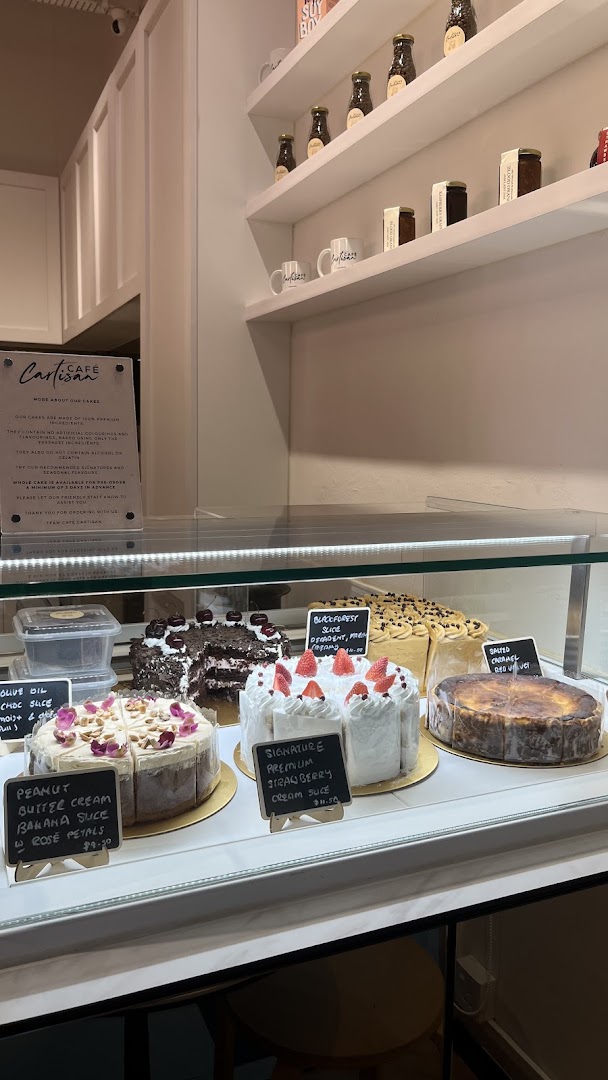 A display case filled with delicious cakes and pastries at Café Cartisan, with retail products on shelves.