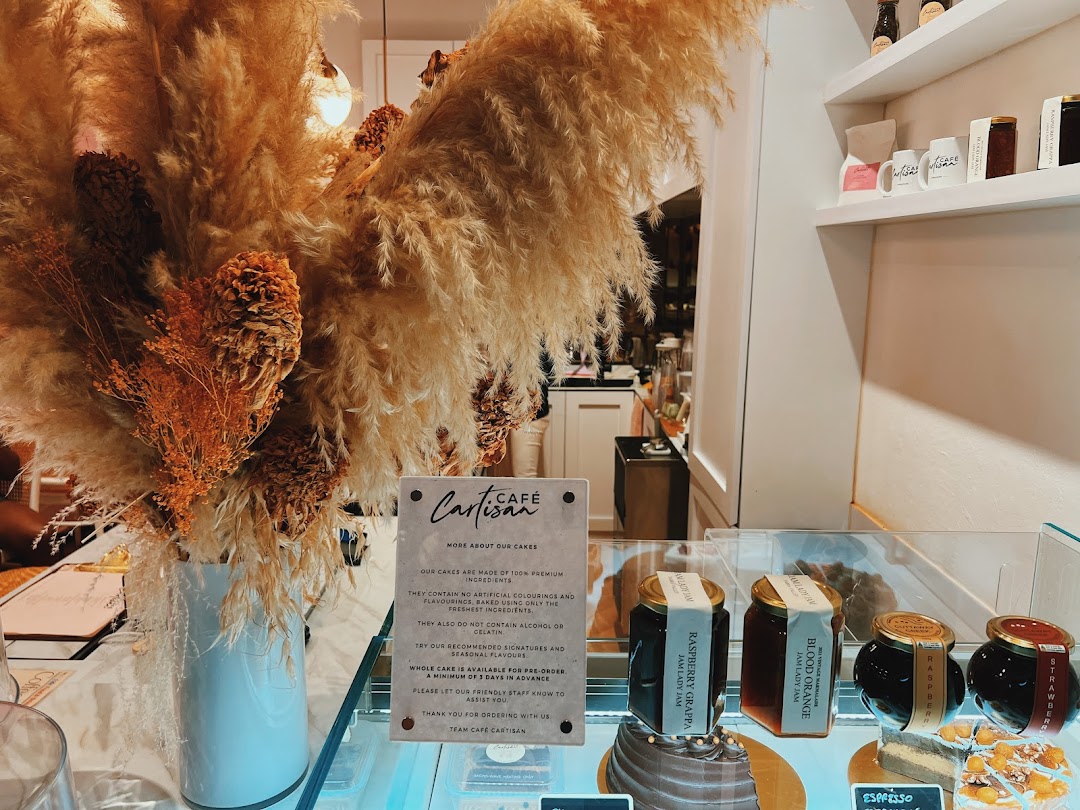 An inviting interior display at Café Cartisan featuring cakes, artisanal jams, and a sign detailing their premium ingredients.
