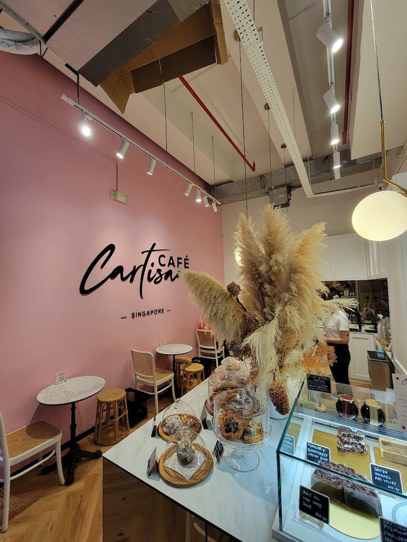 Interior view of Café Cartisan, featuring a pink wall, seating, and a display counter with pastries.