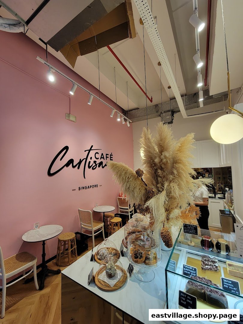 Interior view of Café Cartisan, featuring a pink wall, seating, and a display counter with pastries.