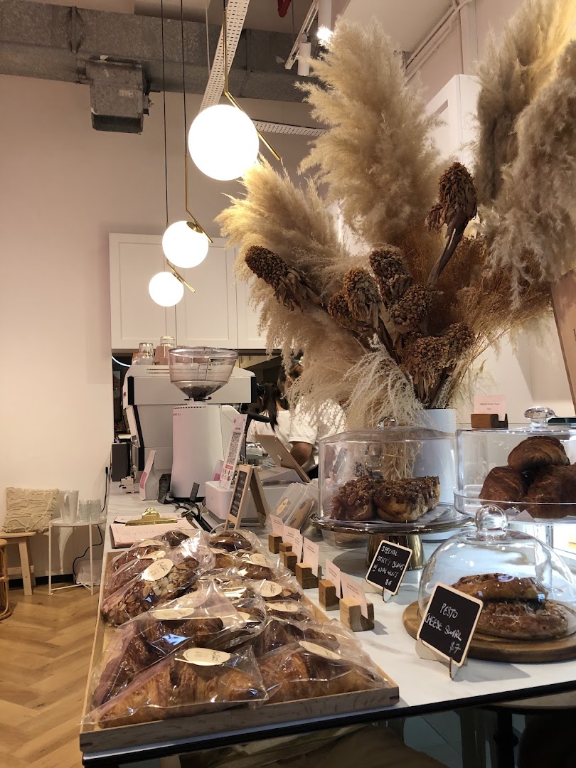 A stylish coffee shop counter displaying fresh pastries, coffee equipment, and decorative pampas grass.