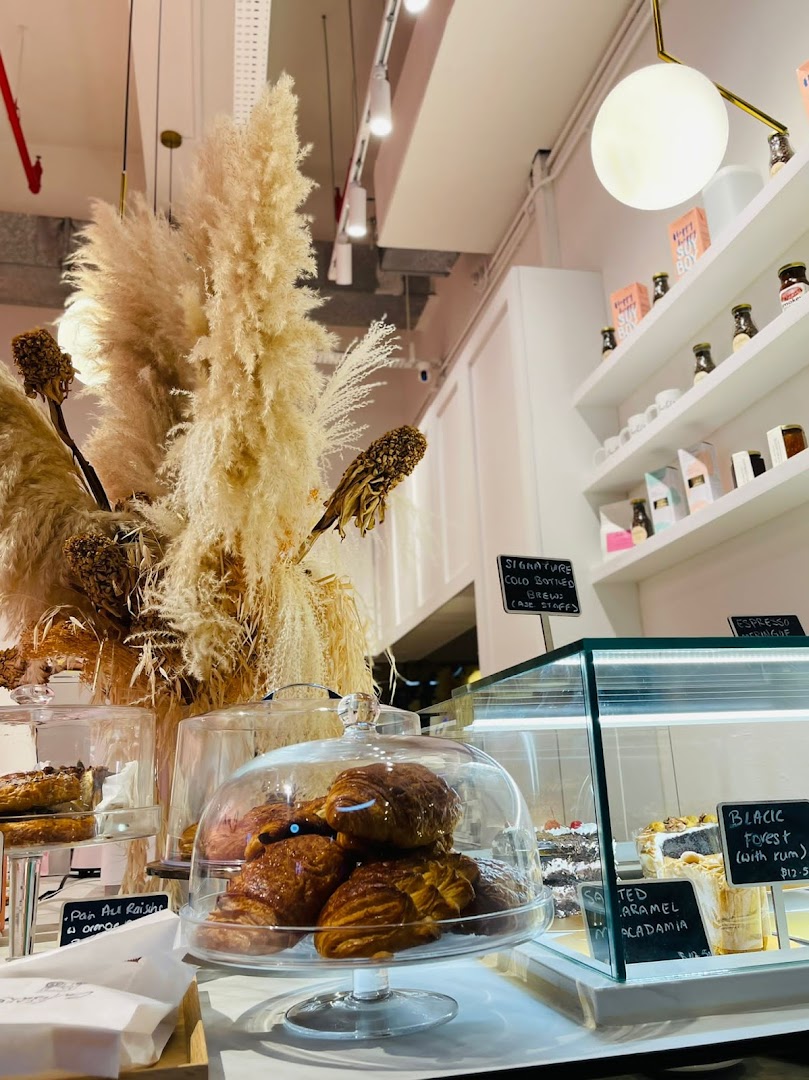 An inviting coffee shop interior showcasing freshly baked pastries, cakes, and specialty coffee items.