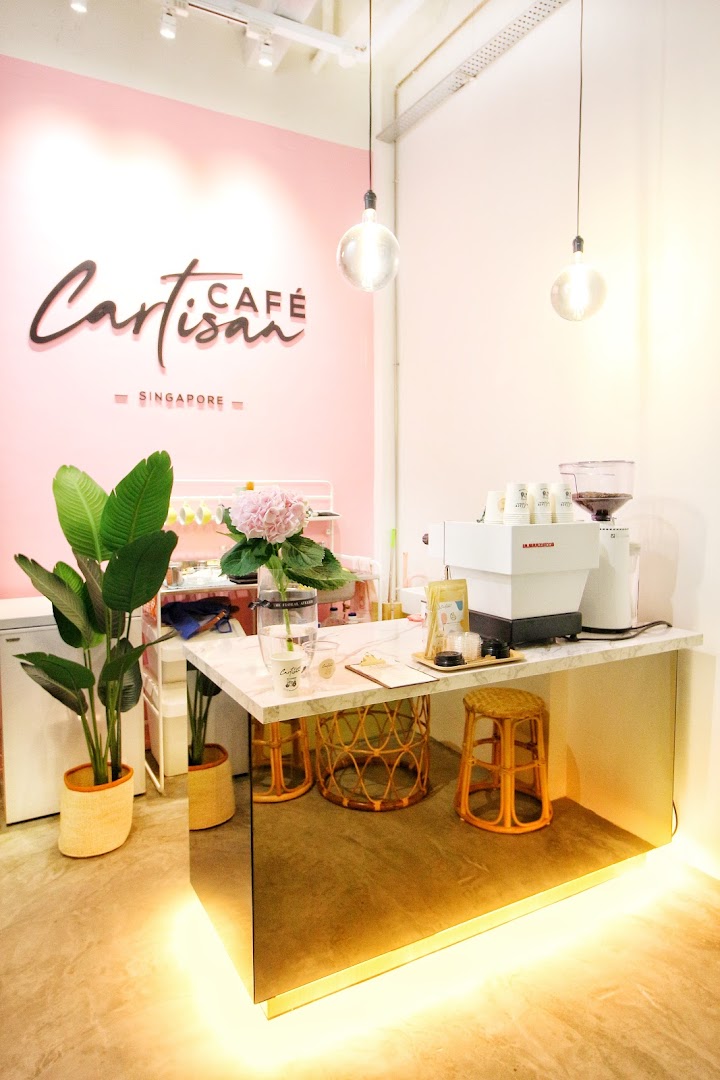 A bright and inviting interior of Café Cartisan, featuring a modern coffee counter with pink walls and lush plants.