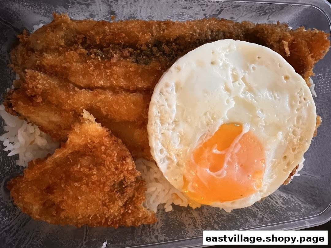 A close-up of a takeout meal featuring crispy fried fish, a sunny-side-up egg, and white rice in a clear container.