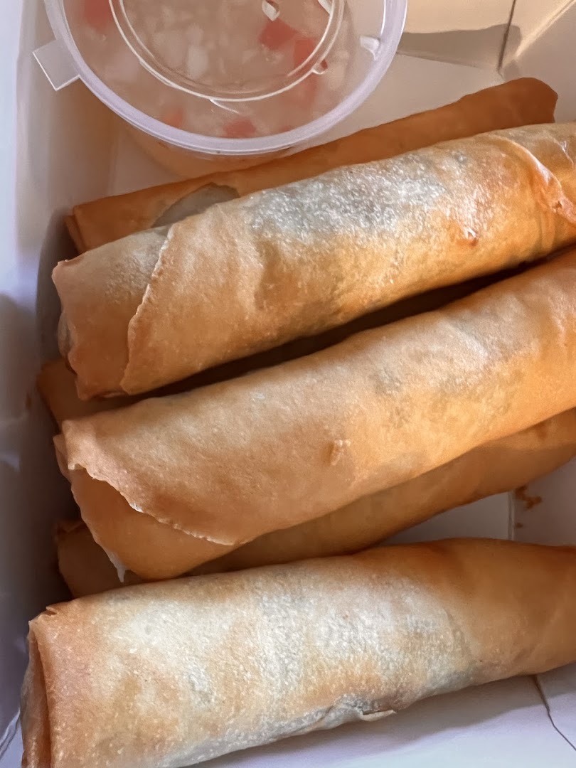 Golden fried spring rolls with a side of dipping sauce in a takeout box from Casa Fiesta.