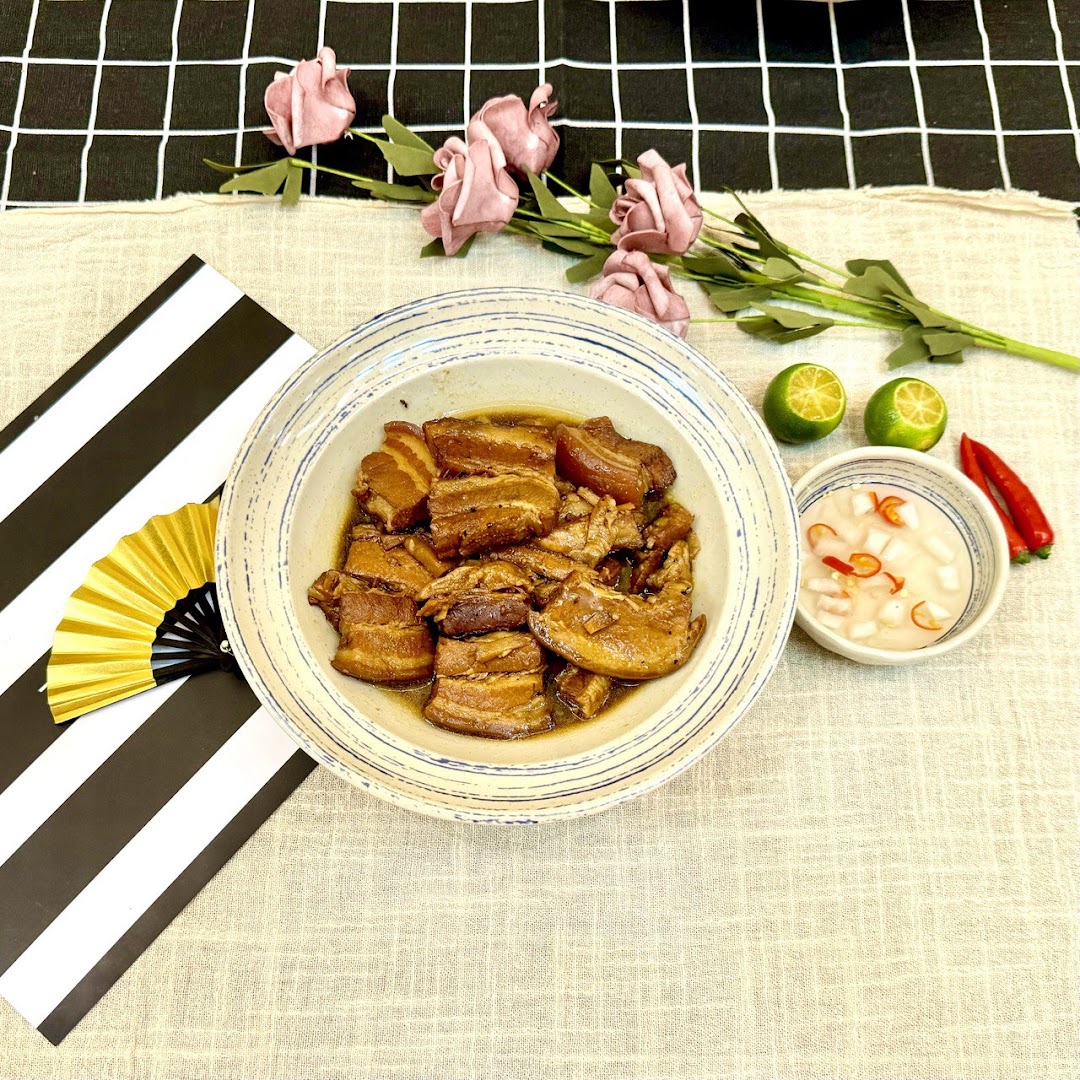 A delicious bowl of braised pork belly with a side of pickled vegetables, limes, and chilies, set on a decorative table.