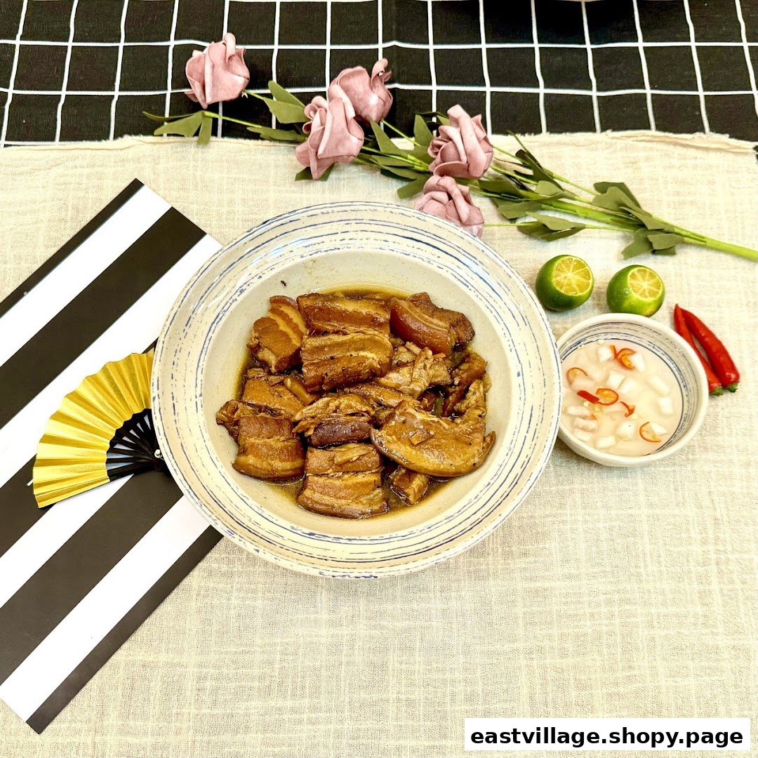 A delicious bowl of braised pork belly with a side of pickled vegetables, limes, and chilies, set on a decorative table.