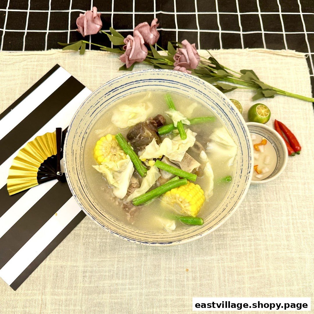 A hearty bowl of soup with meat, corn, green beans, and cabbage, served with lime and chili.