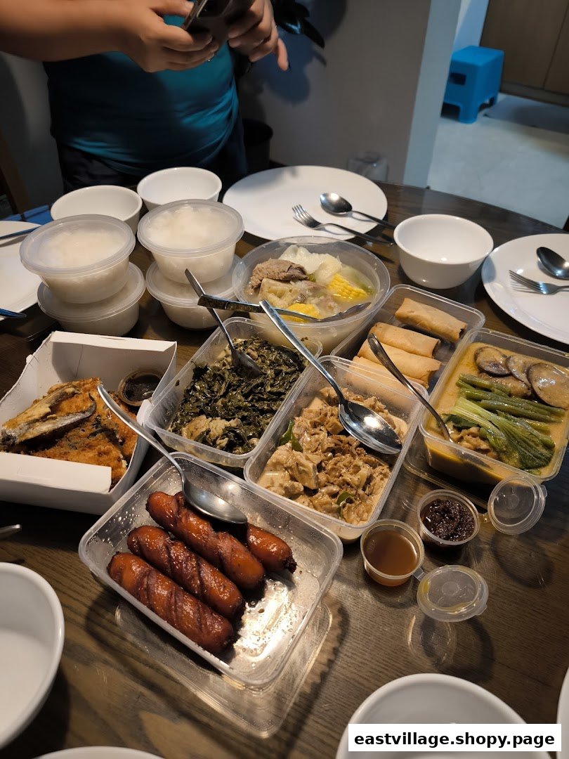 A table filled with various Filipino dishes in takeout containers, including rice, soup, and fried items.