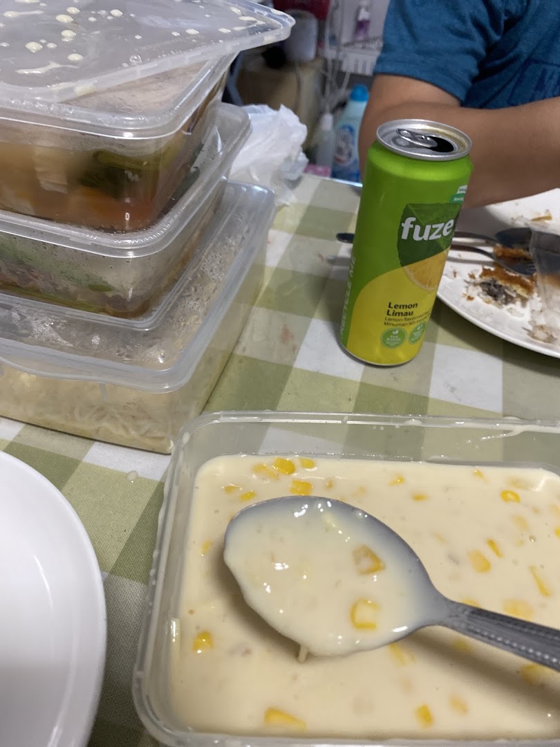 A table with various takeout food containers, a Fuze drink, and a corn dessert.