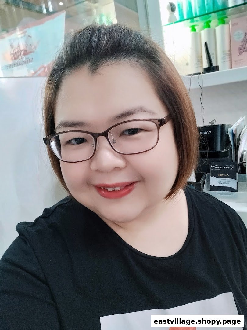 A smiling person wearing glasses, likely staff, inside Charisma Hair Studio with hair products in the background.