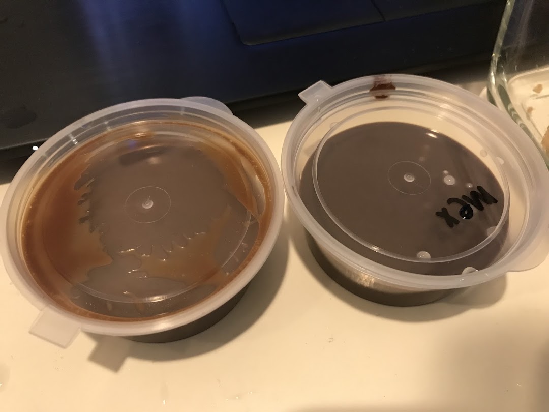 Two plastic containers with lids, one holding a caramel-colored sauce, the other a dark chocolate sauce.