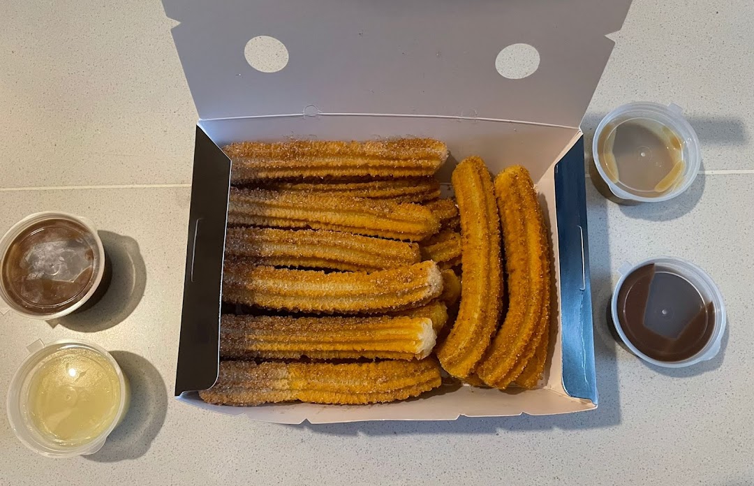 A box of golden churros with three dipping sauces, ready to enjoy.