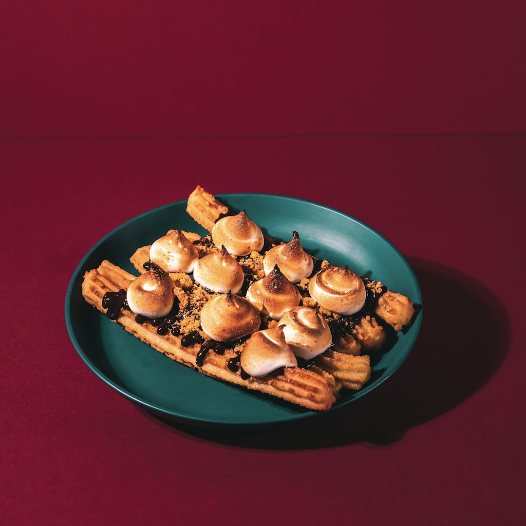 A plate of churros topped with toasted meringue, chocolate drizzle, and cookie crumbs.