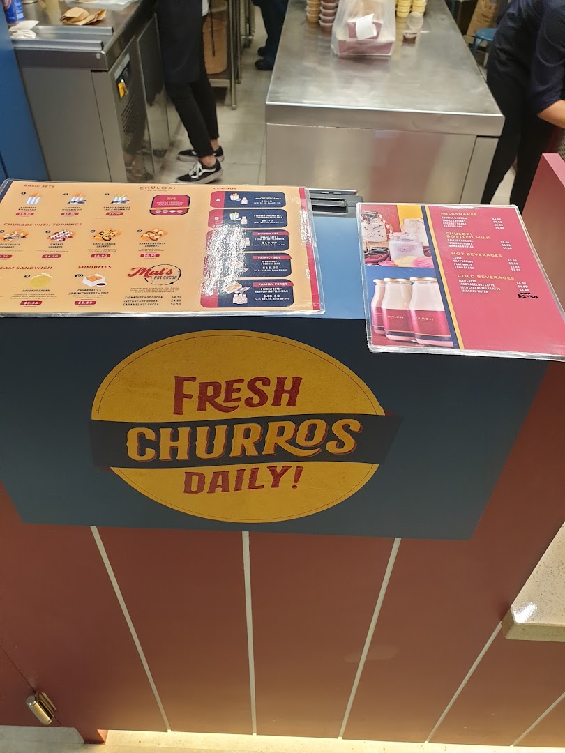A counter at Chulop! by The Syarifs displaying menus for fresh churros, hot cocoa, milkshakes, and other beverages.