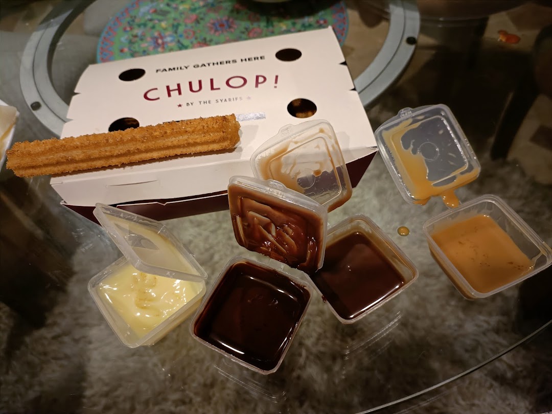 A box of churros with multiple dipping sauces, including chocolate, caramel, and cream, on a glass table.