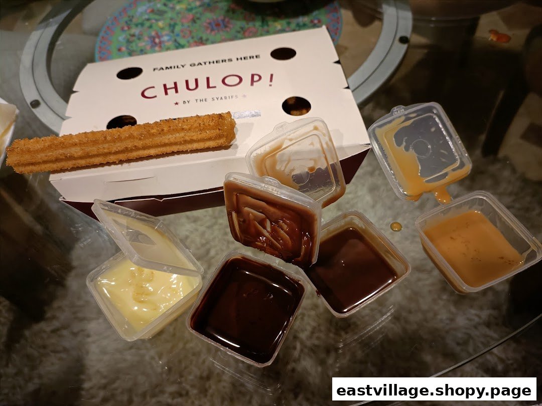 A box of churros with multiple dipping sauces, including chocolate, caramel, and cream, on a glass table.