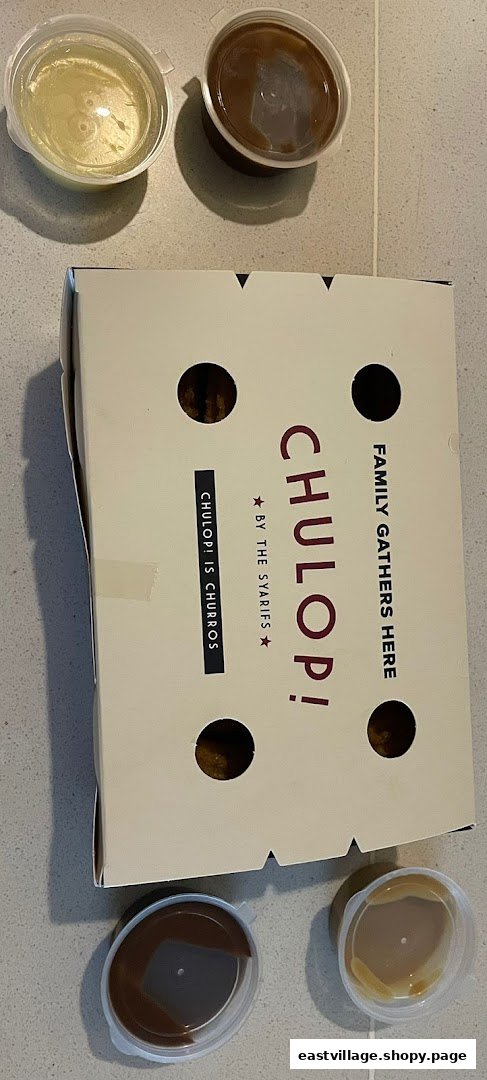 A box of Chulop! churros with four dipping sauces on a tiled surface.