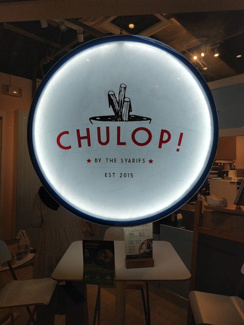Illuminated circular sign for 'Chulop! by The Syarifs' at shop entrance, with interior visible.