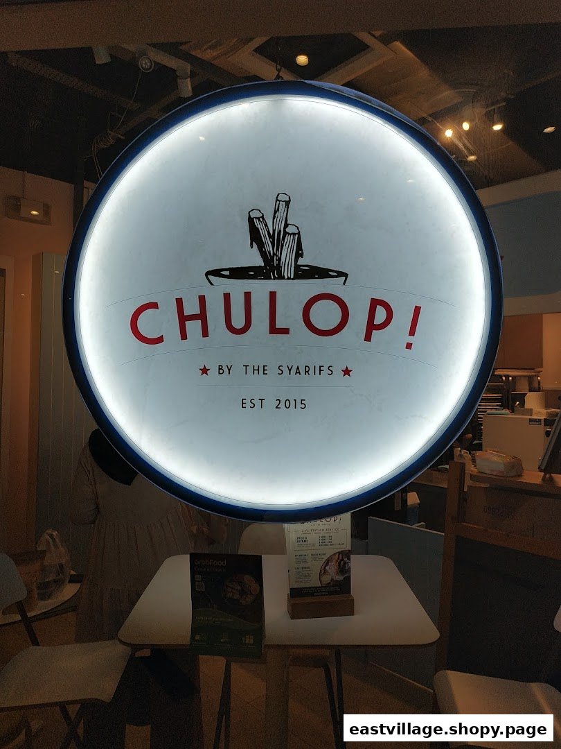 Illuminated circular sign for 'Chulop! by The Syarifs' at shop entrance, with interior visible.