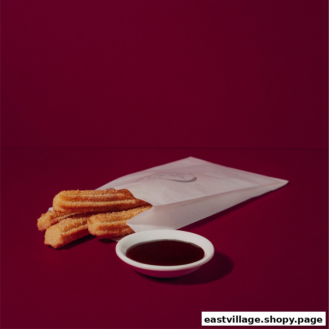 Golden churros in a paper bag with a side of rich chocolate dipping sauce.