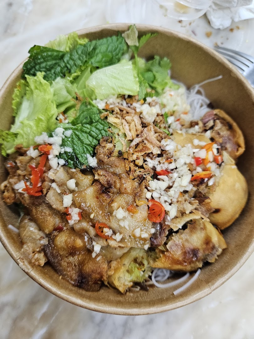 A vibrant bowl of Vietnamese vermicelli noodles with spring rolls, grilled meat, fresh herbs, and toppings.