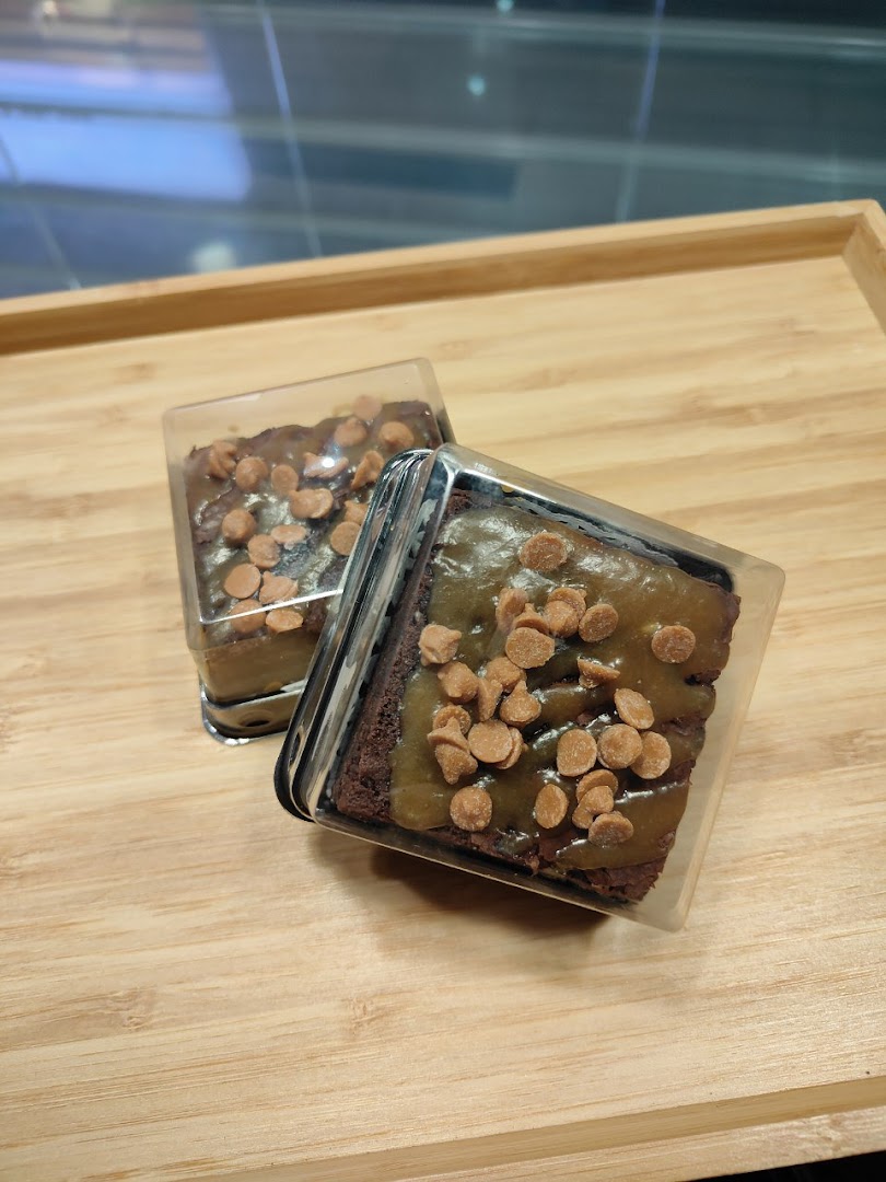 Two delicious caramel brownies with chocolate chips, individually packaged on a wooden tray.