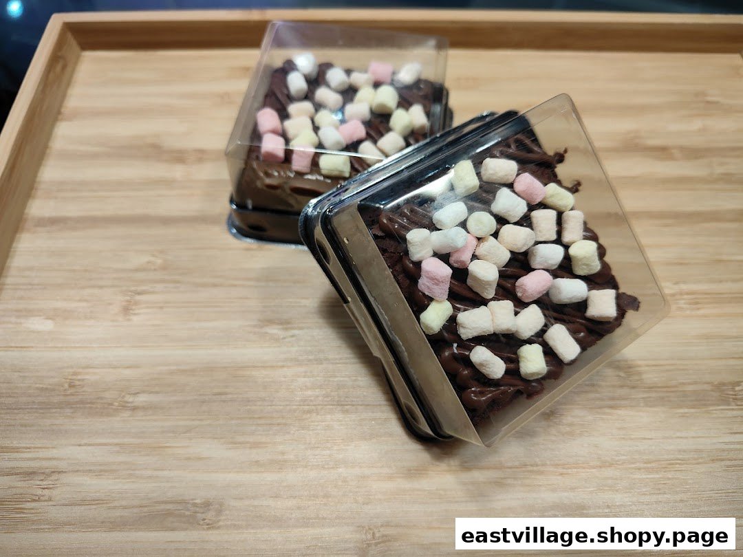 Two delicious chocolate desserts topped with colorful marshmallows in clear packaging on a wooden tray.