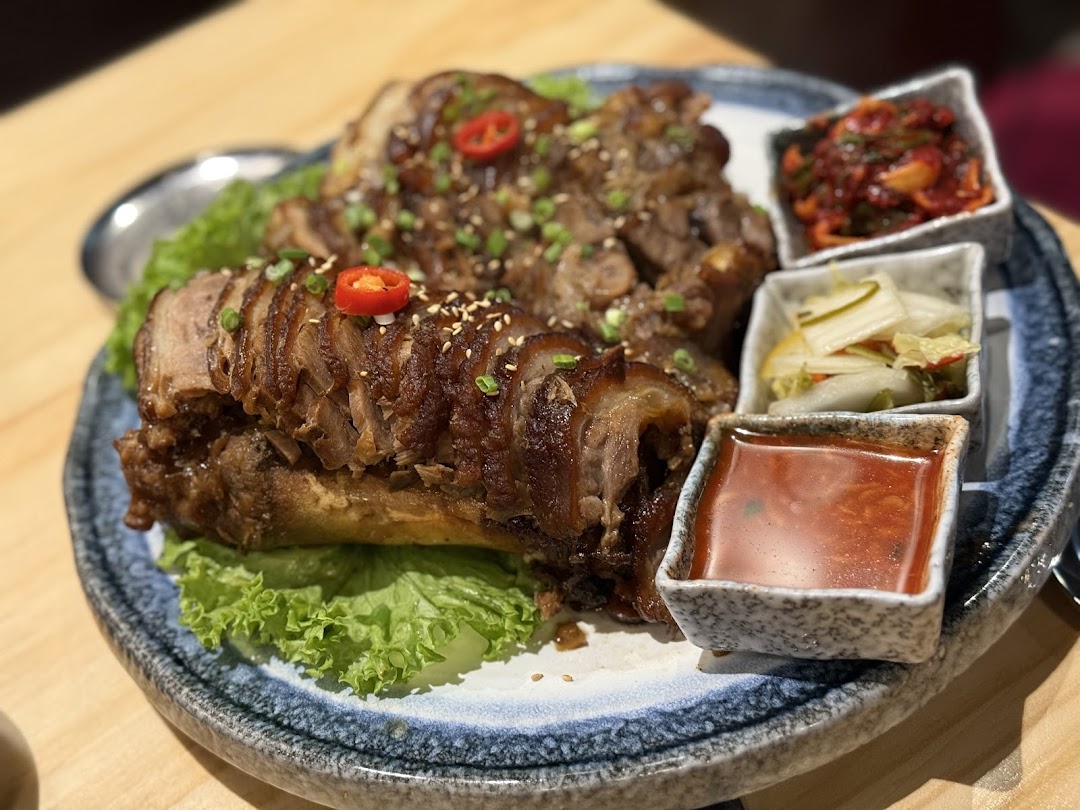 A plate of sliced Korean braised pig's trotters (Jokbal) with side dishes and dipping sauce.