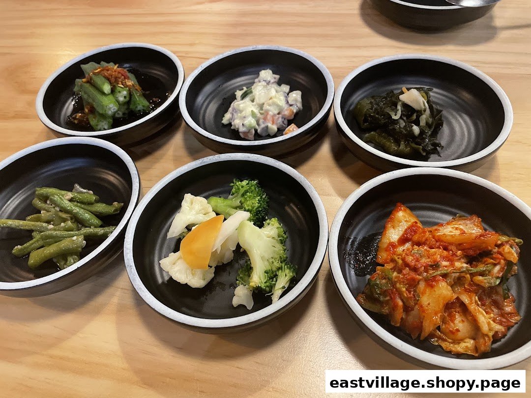 A variety of colorful Korean banchan (side dishes) served in small black bowls on a wooden table.