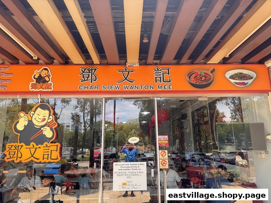 The vibrant orange storefront of Deng Wen Ji, a Char Siew Wanton Mee shop, with its logo and a glimpse of the interior.