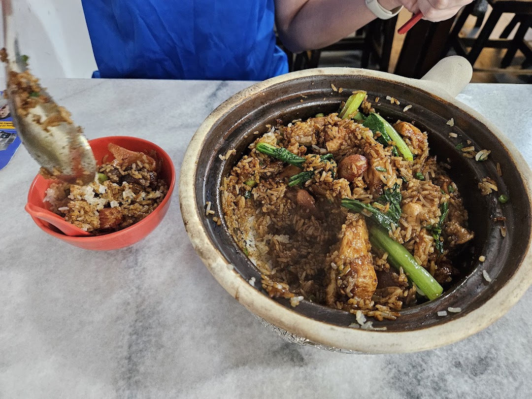 A large claypot of steaming rice with chicken and vegetables is being served into a smaller bowl.