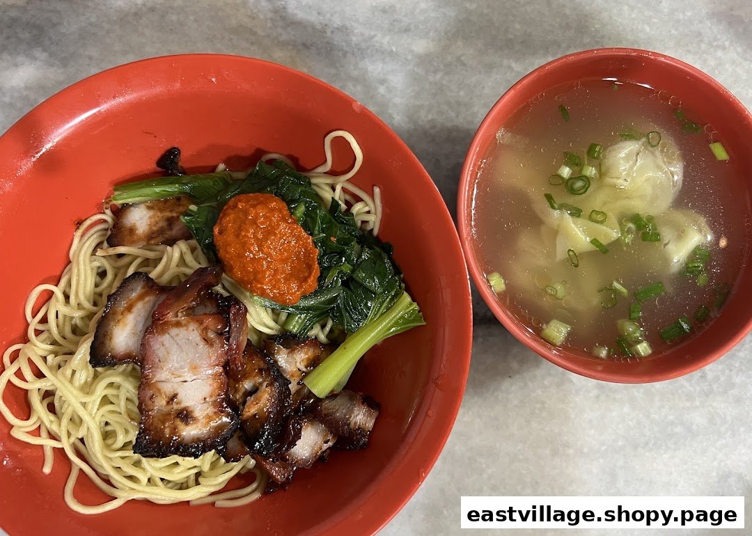 A vibrant bowl of char siu noodles with greens and chili paste, accompanied by a clear wanton soup.