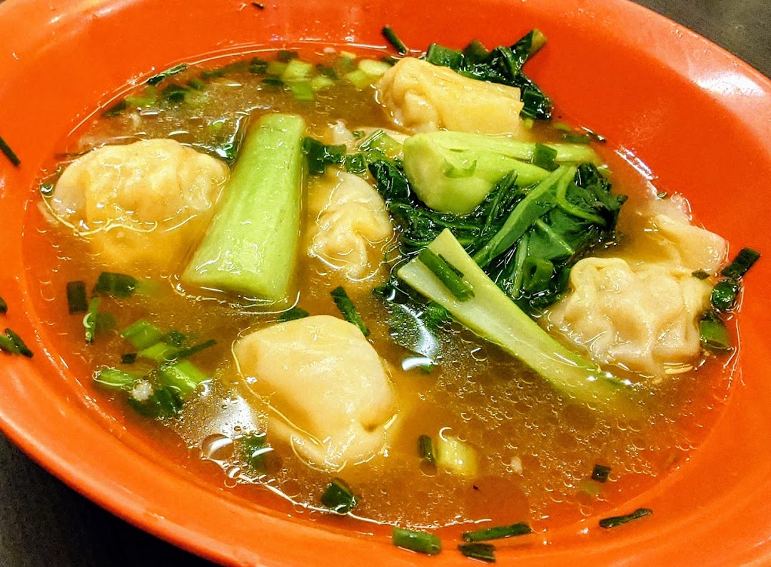 A vibrant orange bowl filled with savory wonton soup, fresh green vegetables, and chopped scallions.
