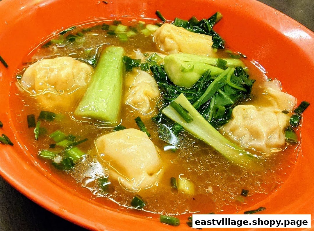 A vibrant orange bowl filled with savory wonton soup, fresh green vegetables, and chopped scallions.