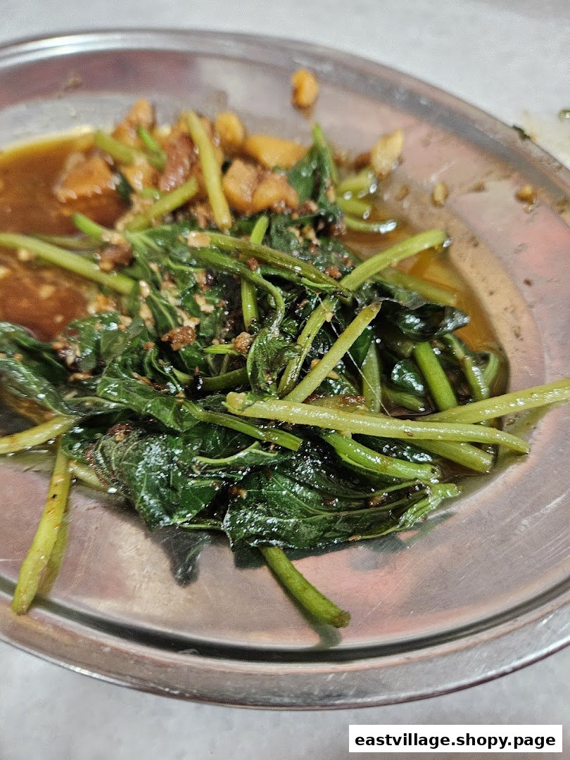 A close-up of a savory stir-fried green vegetable dish with sauce and other ingredients on a metal plate.