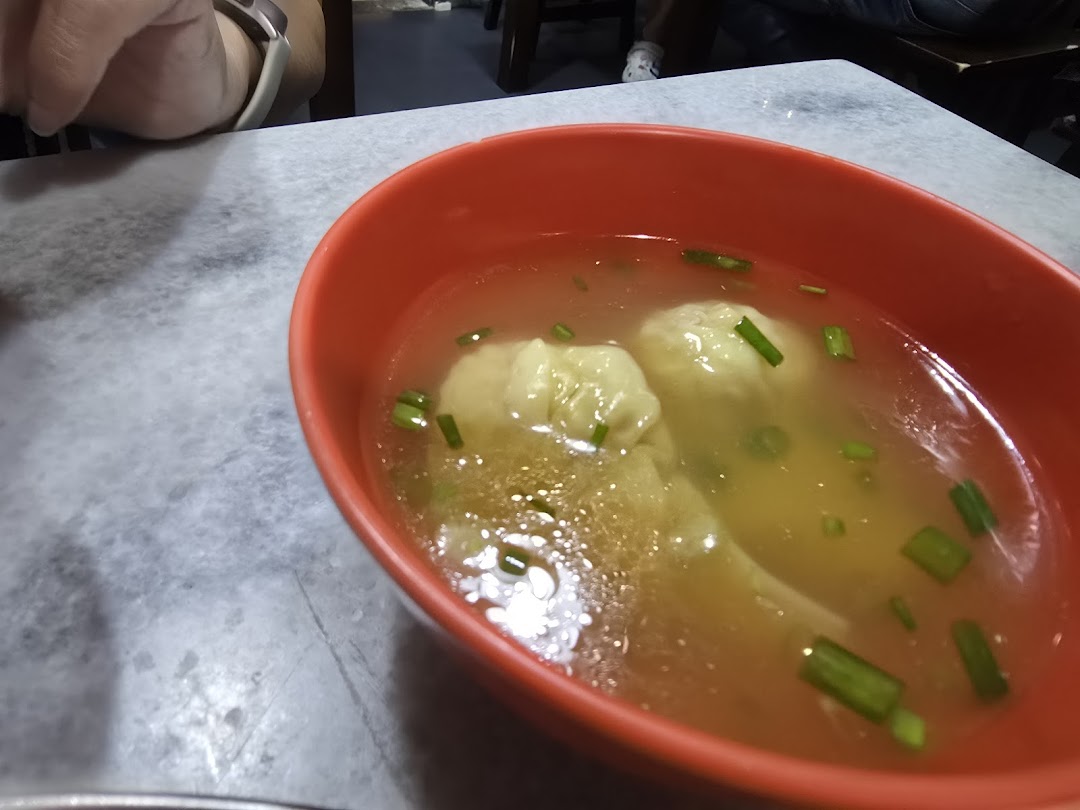 A close-up of a vibrant red bowl filled with clear wonton soup, garnished with green onions.