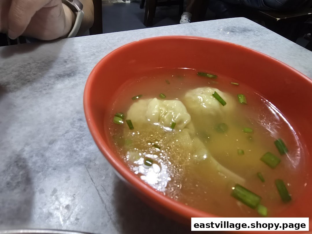A close-up of a vibrant red bowl filled with clear wonton soup, garnished with green onions.