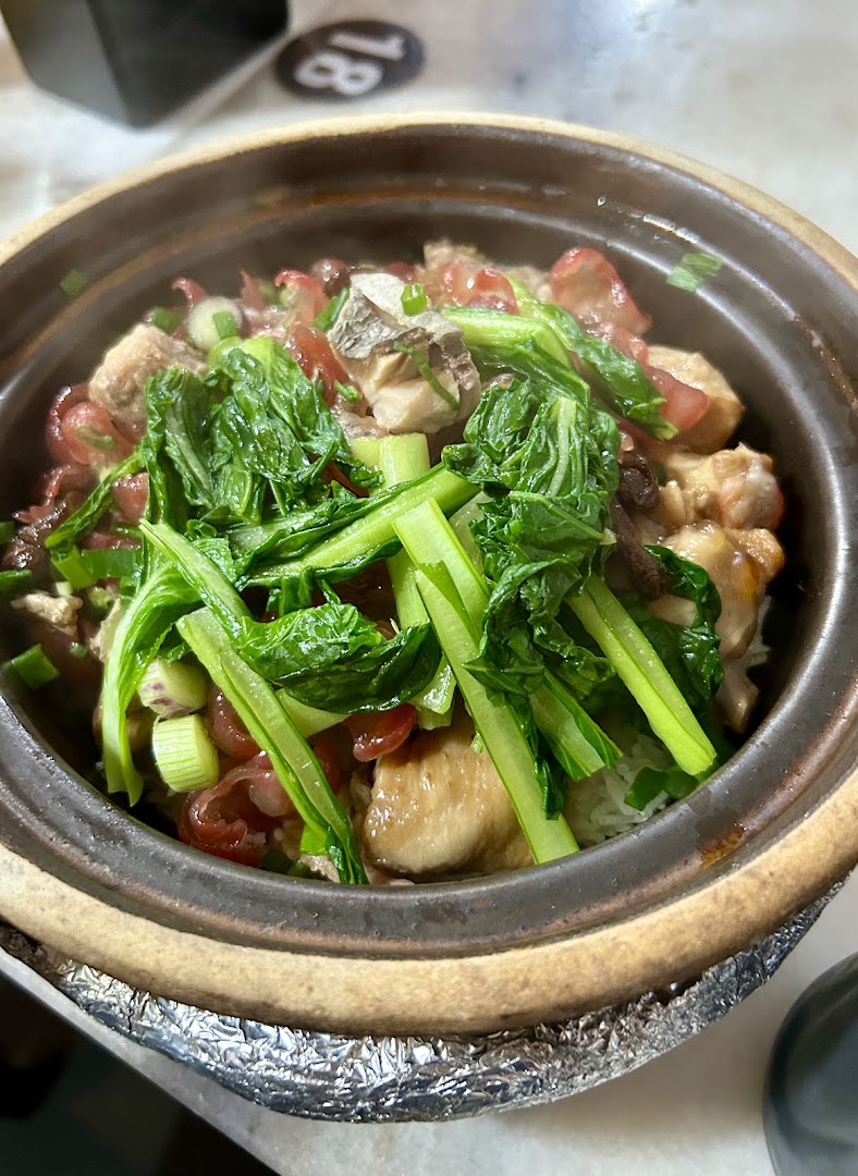 A steaming claypot rice dish with chicken, Chinese sausage, and green vegetables.