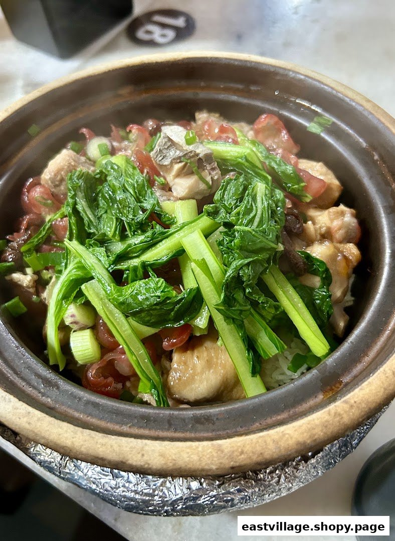 A steaming claypot rice dish with chicken, Chinese sausage, and green vegetables.
