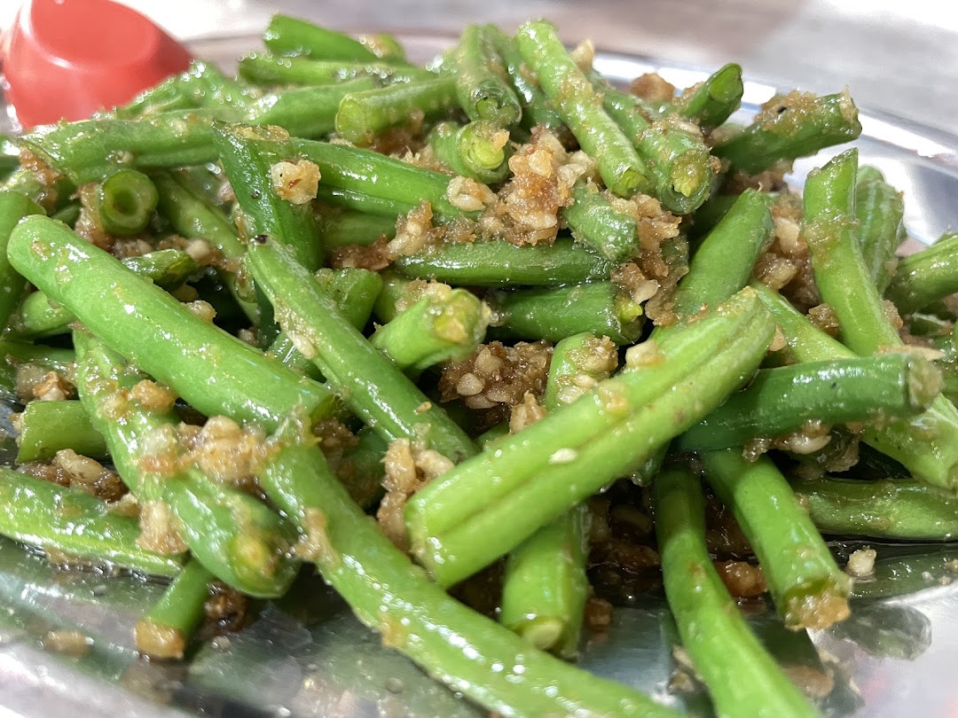A close-up of vibrant green beans stir-fried with savory minced garlic on a metal plate.