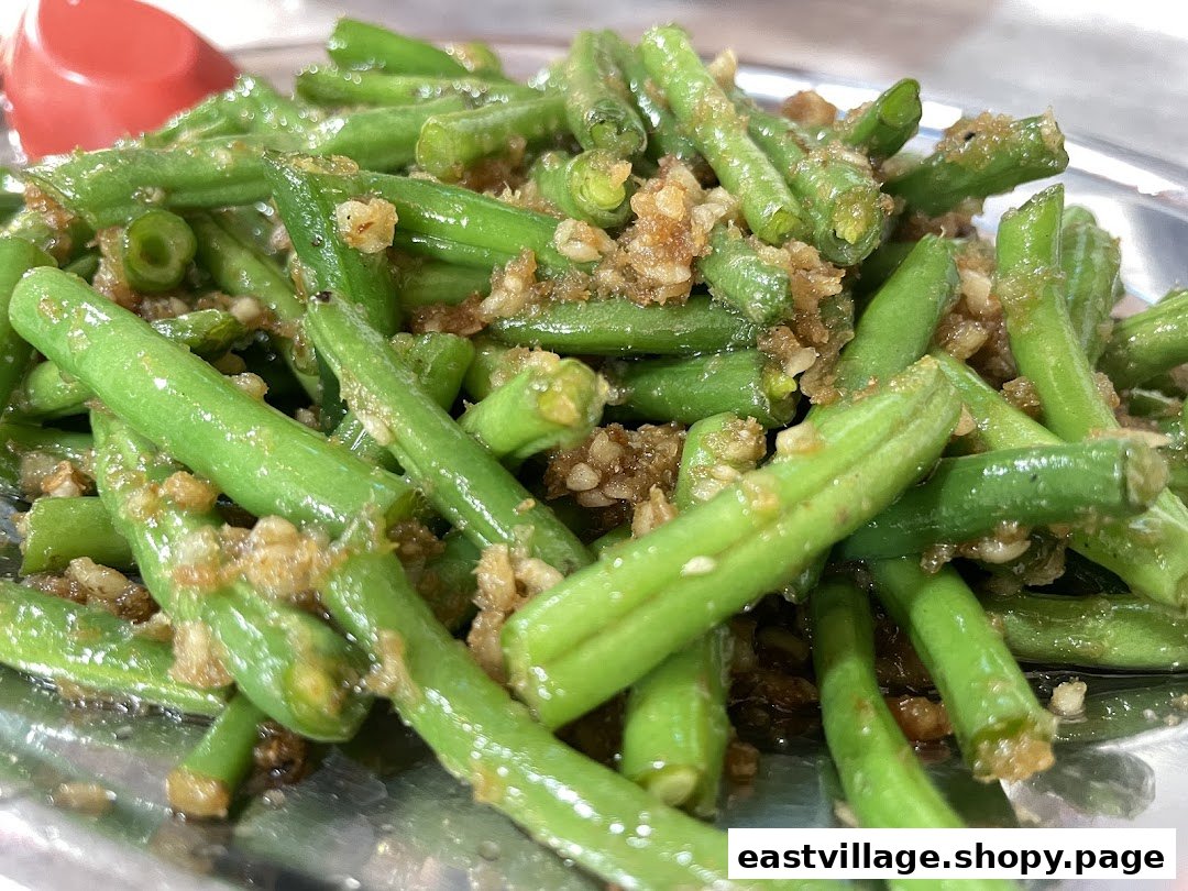 A close-up of vibrant green beans stir-fried with savory minced garlic on a metal plate.
