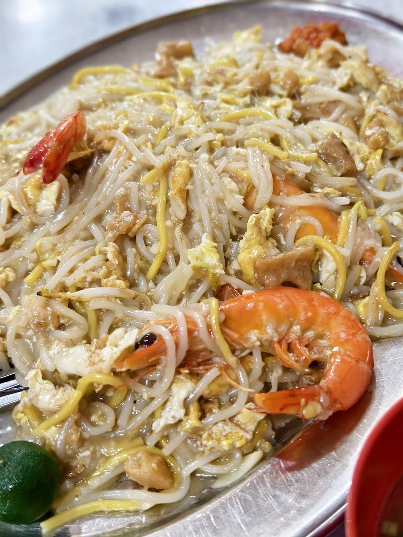 A close-up of a plate of Hokkien Mee with prawns, eggs, and a lime wedge.